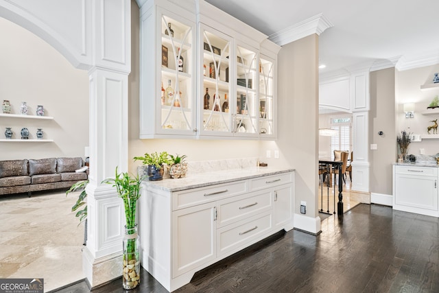 bar featuring decorative columns, baseboards, arched walkways, dark wood-type flooring, and crown molding