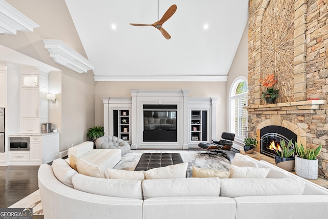 living area with ceiling fan, high vaulted ceiling, a stone fireplace, dark wood-style flooring, and crown molding