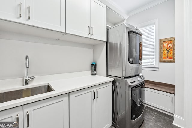 laundry room with dark tile patterned floors, stacked washer / dryer, a sink, cabinet space, and crown molding