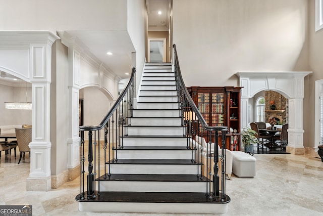 staircase featuring arched walkways, marble finish floor, a towering ceiling, and decorative columns