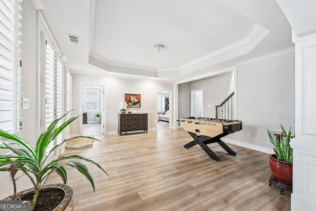 exercise area featuring visible vents, light wood-type flooring, a raised ceiling, and a wealth of natural light