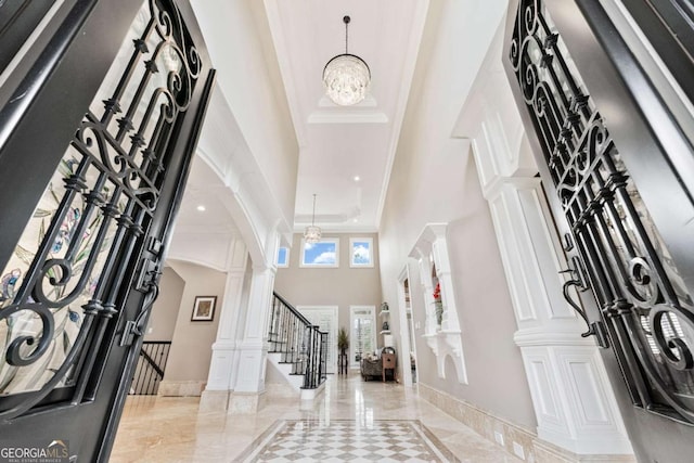 entryway with a notable chandelier, a high ceiling, stairway, ornate columns, and crown molding