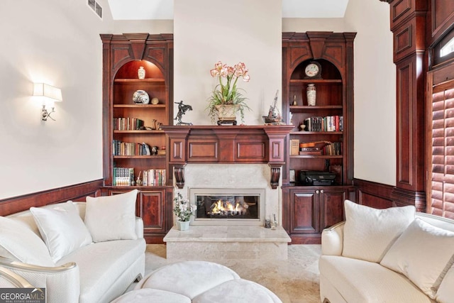 living area featuring wainscoting, visible vents, built in features, and a high end fireplace