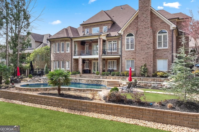 back of house featuring a chimney, a patio area, brick siding, and a balcony