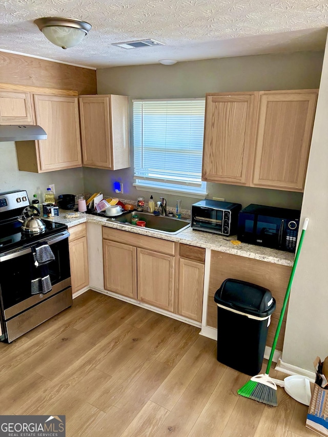 kitchen with light wood finished floors, stainless steel electric range, light brown cabinetry, black microwave, and a sink