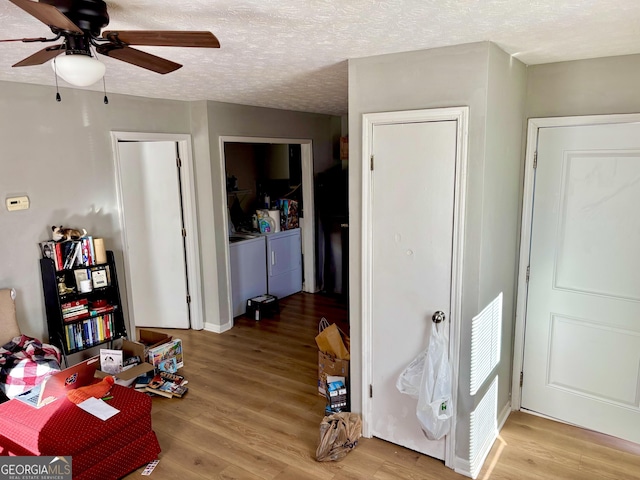 interior space with a textured ceiling, ceiling fan, independent washer and dryer, and wood finished floors