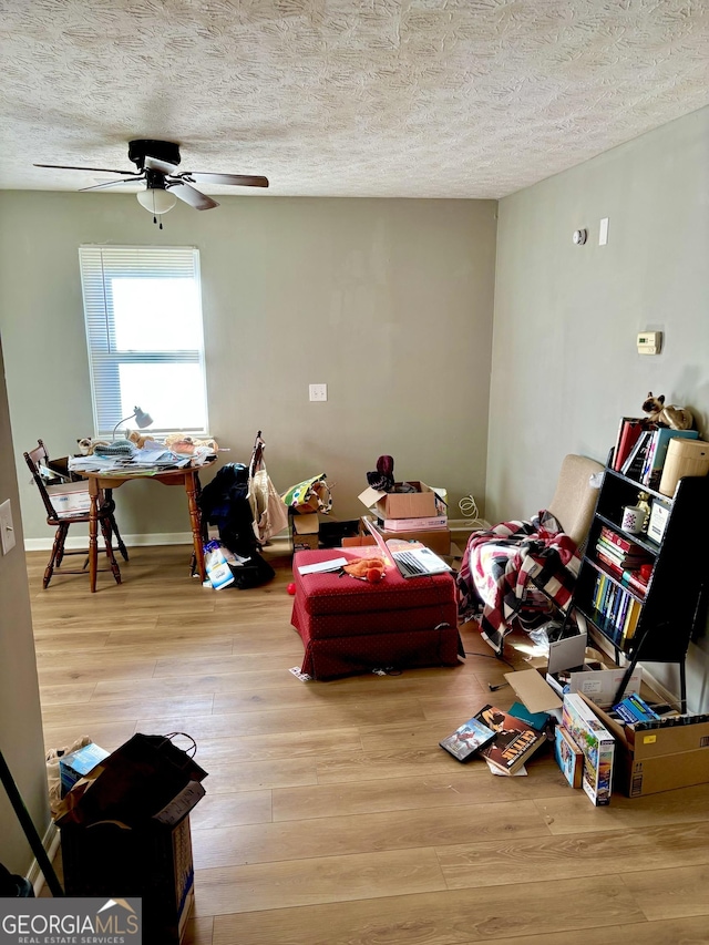 interior space with baseboards, a textured ceiling, a ceiling fan, and wood finished floors