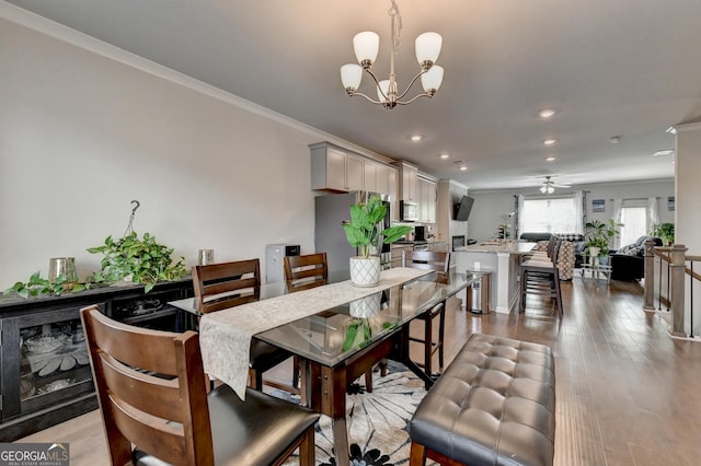 dining area featuring ceiling fan with notable chandelier, wood finished floors, and ornamental molding