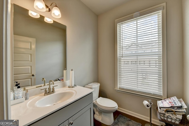 bathroom with baseboards, toilet, a healthy amount of sunlight, and vanity