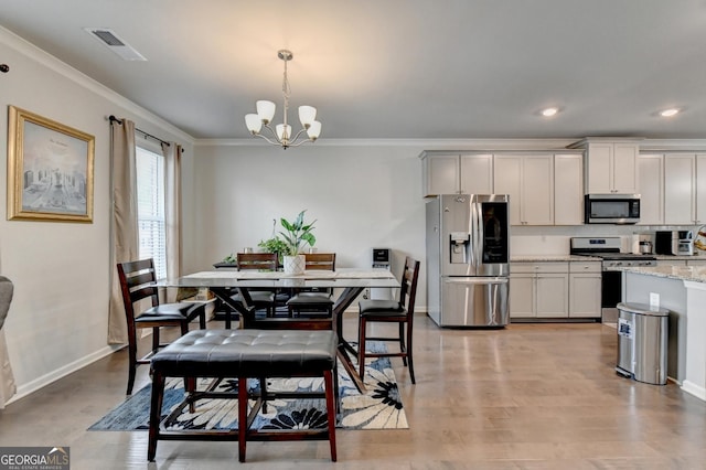 dining room featuring baseboards, visible vents, light wood-style flooring, ornamental molding, and a chandelier