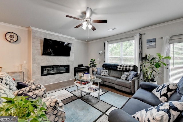 living area featuring a tiled fireplace, wood finished floors, visible vents, and ornamental molding