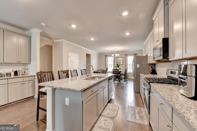 kitchen featuring a breakfast bar, ornamental molding, appliances with stainless steel finishes, light wood-style floors, and a sink