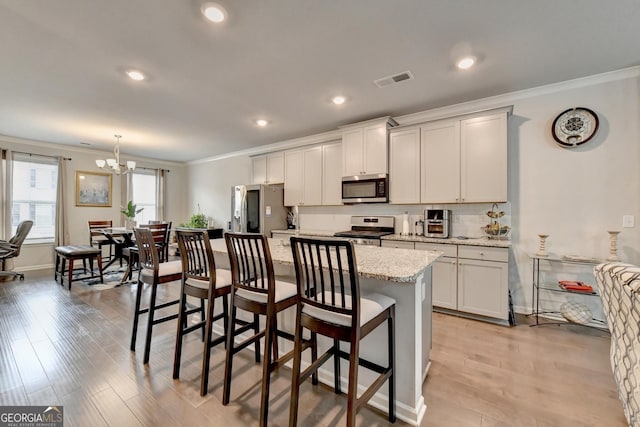 kitchen featuring a kitchen island, ornamental molding, stainless steel appliances, light wood-style floors, and a kitchen breakfast bar