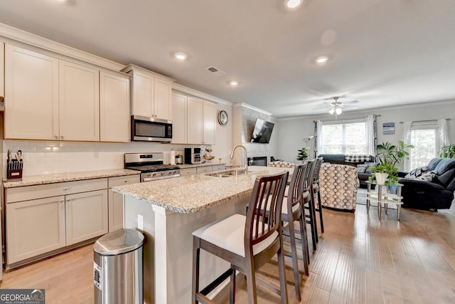 kitchen featuring ornamental molding, a sink, open floor plan, stainless steel appliances, and light wood finished floors