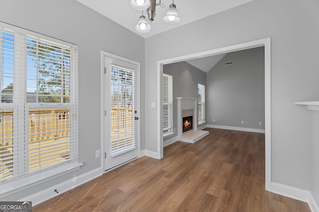 interior space featuring a warm lit fireplace, a notable chandelier, wood finished floors, visible vents, and baseboards