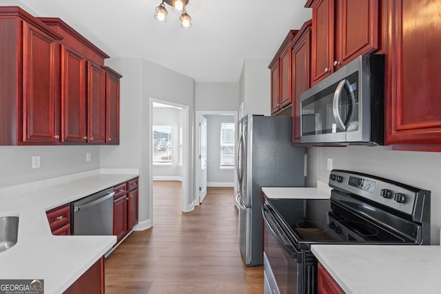 kitchen featuring reddish brown cabinets, baseboards, stainless steel appliances, and wood finished floors