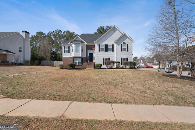 raised ranch featuring fence, a front lawn, and brick siding