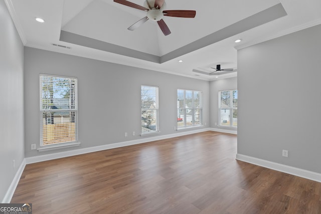 empty room with wood finished floors, a raised ceiling, visible vents, and a healthy amount of sunlight