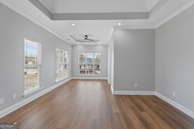 spare room with ornamental molding, a tray ceiling, wood finished floors, and baseboards