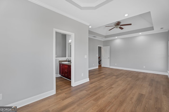 empty room with a sink, wood finished floors, baseboards, a raised ceiling, and crown molding