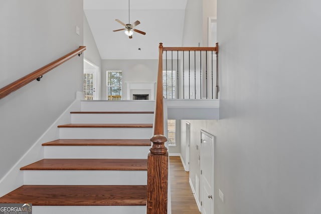 stairway with high vaulted ceiling, a fireplace, wood finished floors, and a ceiling fan