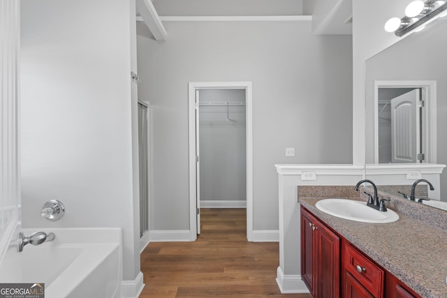 full bathroom with a stall shower, wood finished floors, a walk in closet, vanity, and a bath