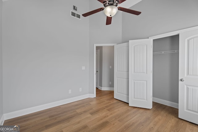 unfurnished bedroom featuring a closet, visible vents, a high ceiling, wood finished floors, and baseboards