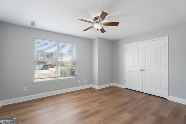 unfurnished bedroom with baseboards, visible vents, a ceiling fan, wood finished floors, and a closet