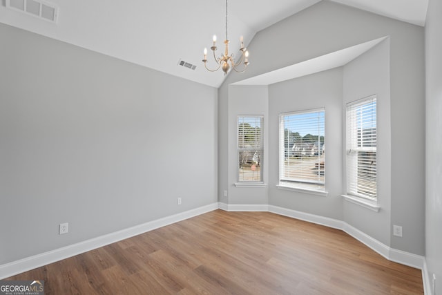 empty room with a chandelier, wood finished floors, visible vents, and baseboards