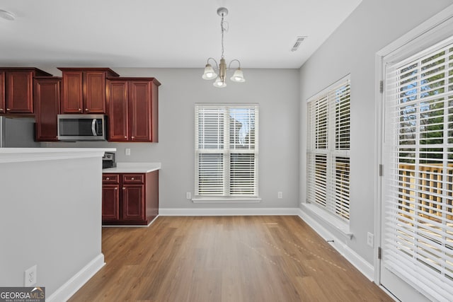 kitchen with dark brown cabinets, light wood finished floors, stainless steel microwave, and hanging light fixtures