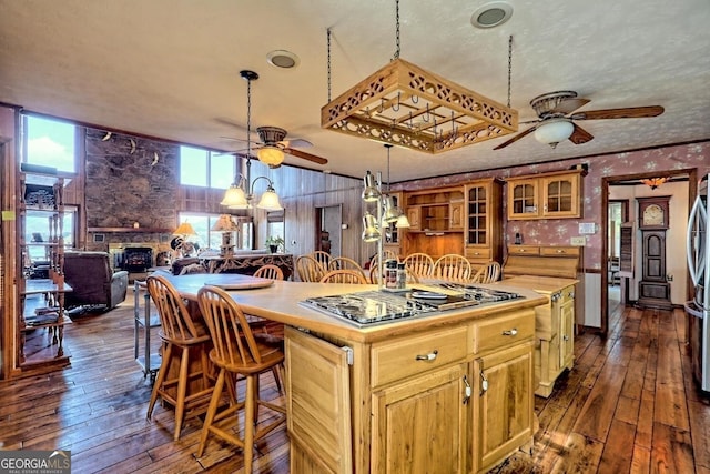 kitchen with a ceiling fan, dark wood finished floors, a stone fireplace, and wallpapered walls