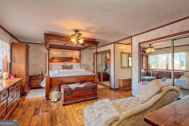 bedroom featuring multiple closets, wood-type flooring, crown molding, and wallpapered walls