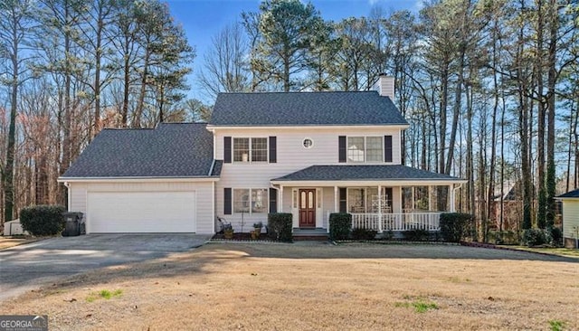 colonial home featuring a chimney, concrete driveway, covered porch, an attached garage, and a front yard