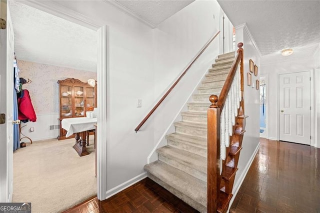 stairs with wainscoting, crown molding, a textured ceiling, and wallpapered walls