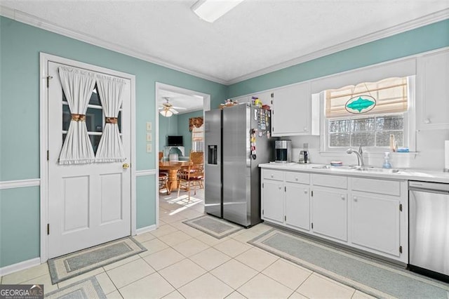 kitchen featuring light countertops, appliances with stainless steel finishes, ornamental molding, white cabinets, and a sink