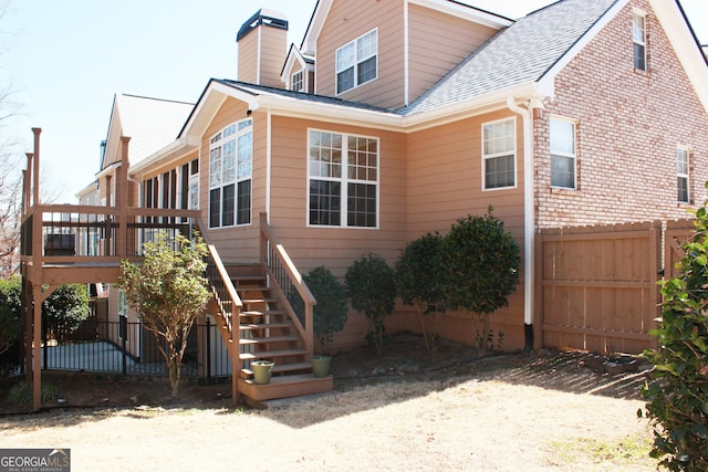 exterior space with roof with shingles, a chimney, stairway, fence, and a wooden deck