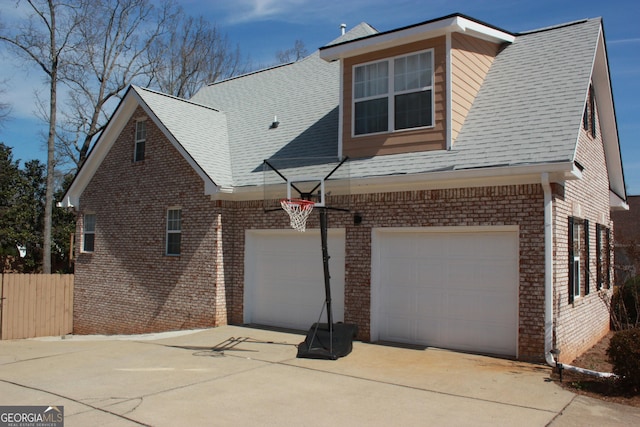 view of side of home featuring brick siding, a shingled roof, concrete driveway, fence, and a garage