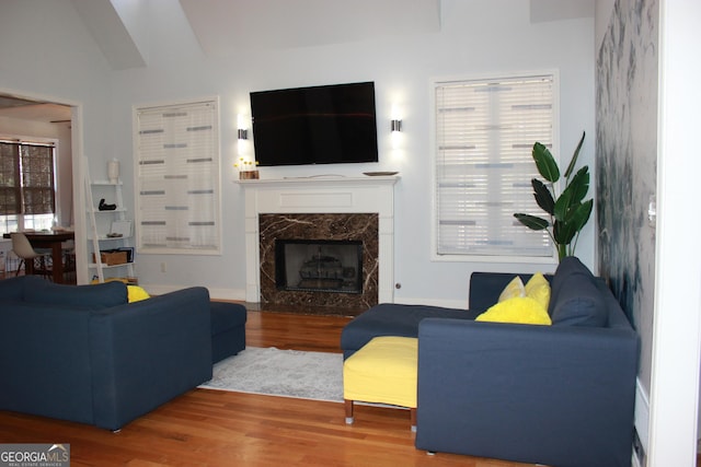 living room featuring a premium fireplace, vaulted ceiling, and wood finished floors