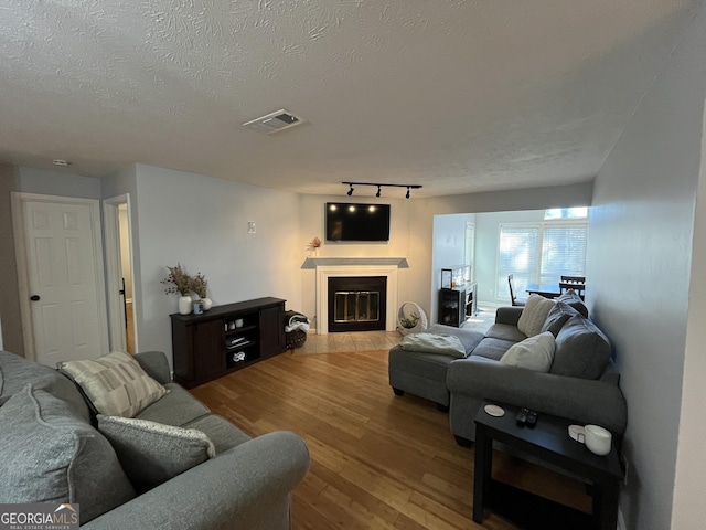 living area featuring a textured ceiling, wood finished floors, visible vents, a glass covered fireplace, and rail lighting