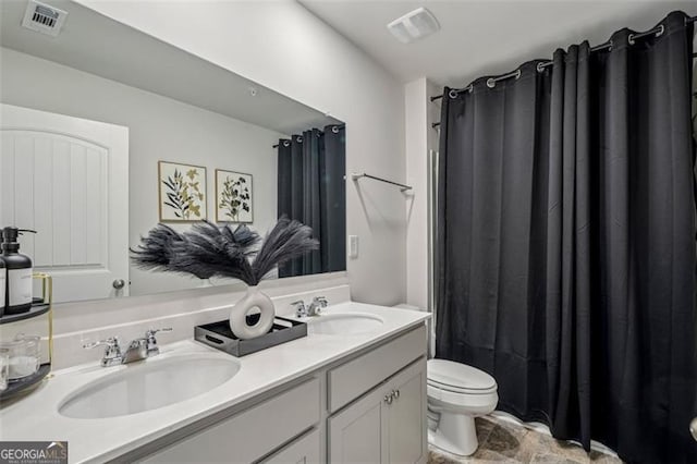 bathroom with visible vents, double vanity, a sink, and toilet