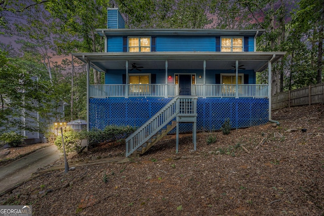 view of front facade featuring a chimney, covered porch, a ceiling fan, fence, and stairs