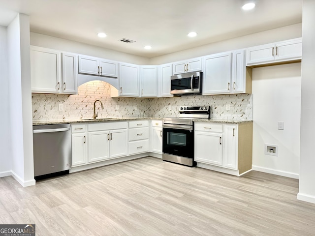 kitchen featuring visible vents, light wood-style flooring, appliances with stainless steel finishes, light stone countertops, and a sink