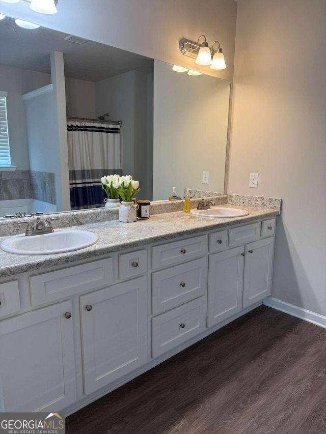 bathroom featuring a bathtub, double vanity, a sink, and wood finished floors