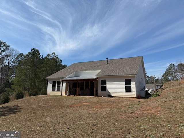 rear view of house with roof with shingles and a yard