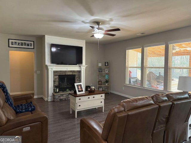 living room with baseboards, dark wood finished floors, a ceiling fan, and a stone fireplace