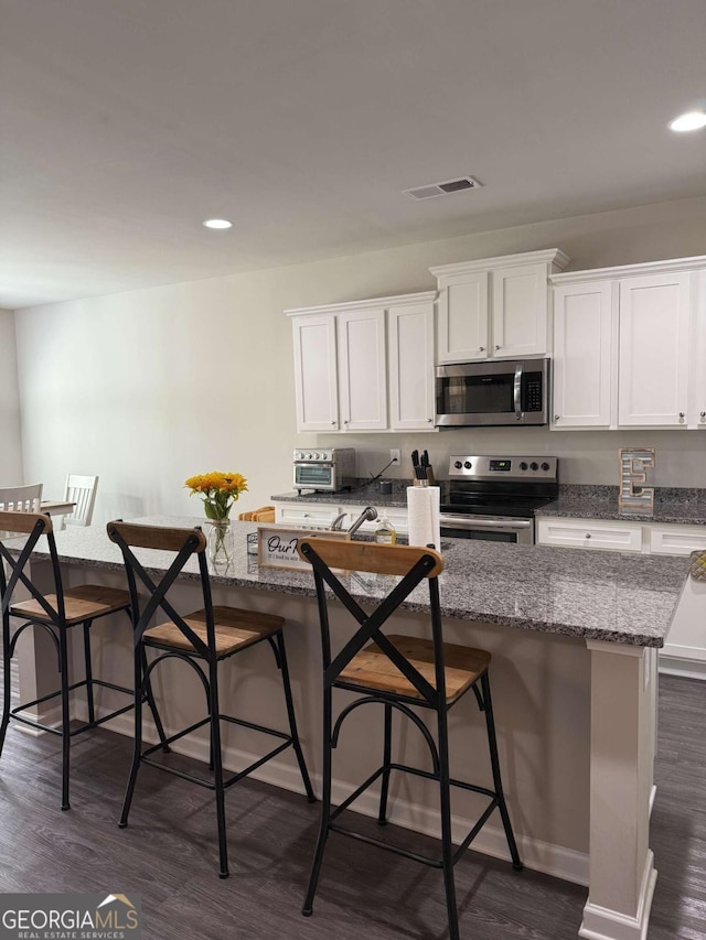 kitchen featuring stainless steel appliances, dark wood-style flooring, visible vents, and white cabinetry