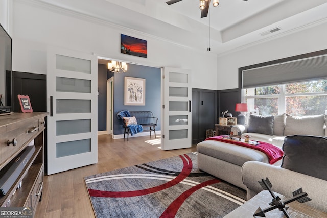 living room featuring a tray ceiling, visible vents, ornamental molding, light wood-type flooring, and ceiling fan with notable chandelier