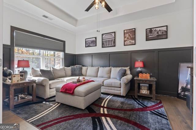 living area featuring a tray ceiling, visible vents, a decorative wall, wainscoting, and wood finished floors