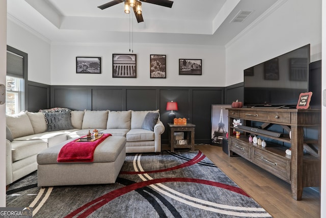 living area with a tray ceiling, wainscoting, wood finished floors, and visible vents