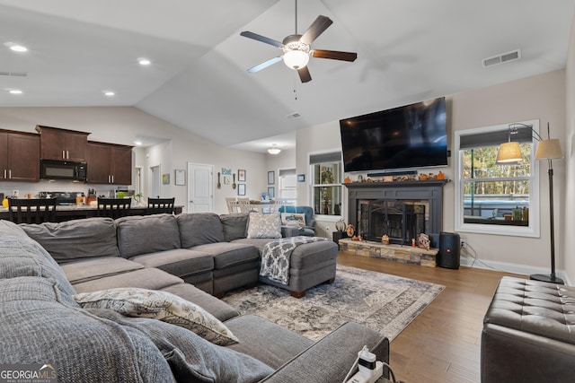 living room with lofted ceiling, a stone fireplace, wood finished floors, and visible vents